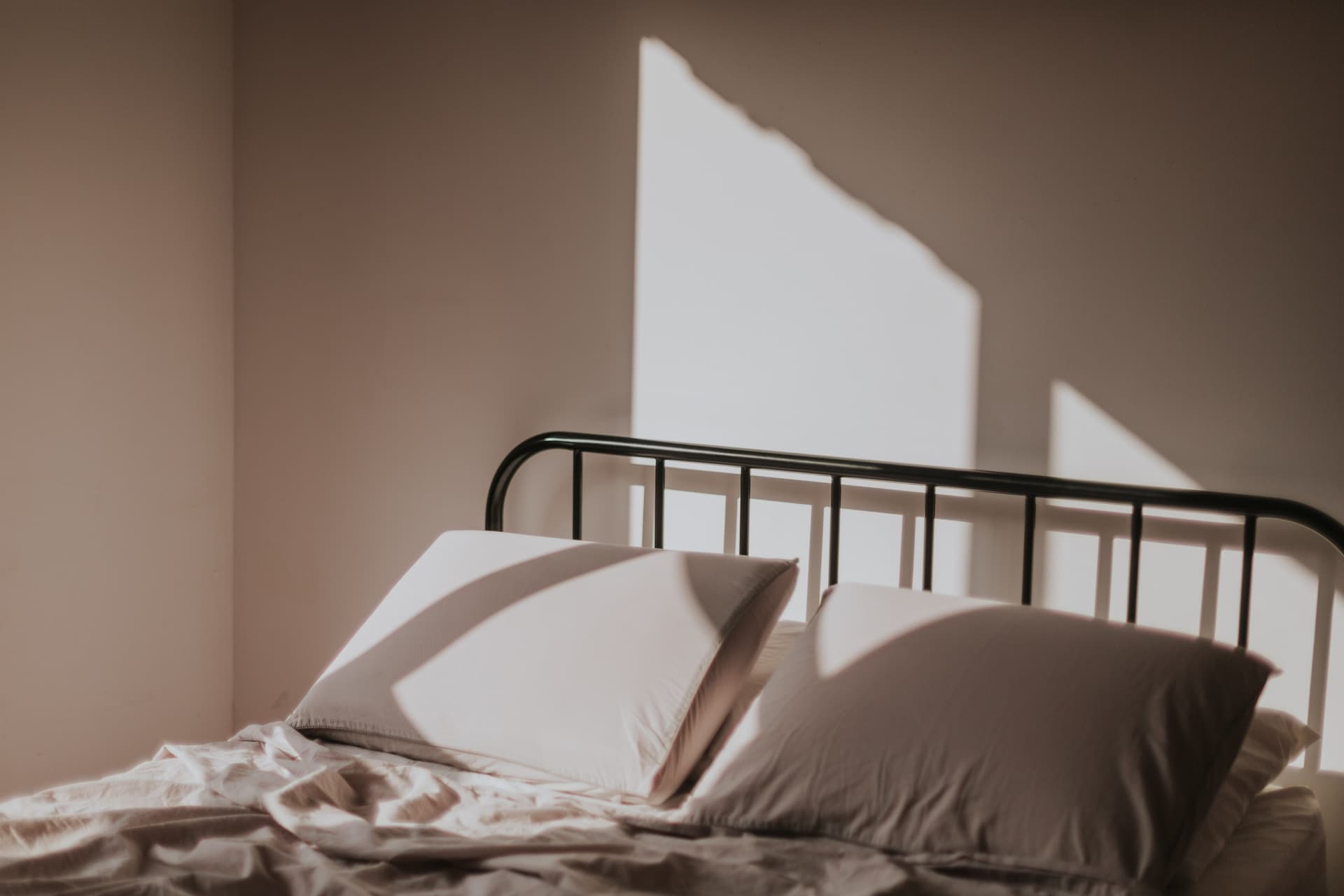 Morning light throwing shadows across a neatly made bed with a black metal headboard