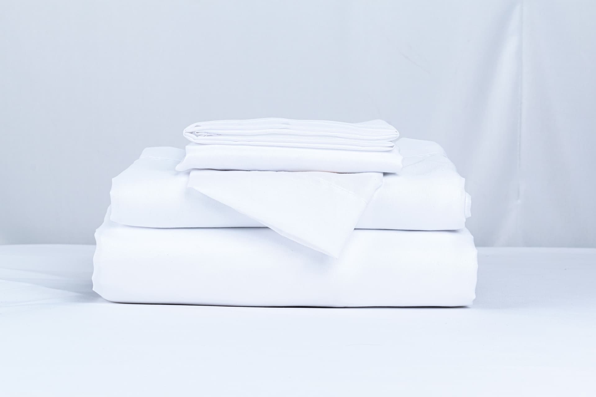 A neatly folded stack of crisp white bed linens on a clean surface