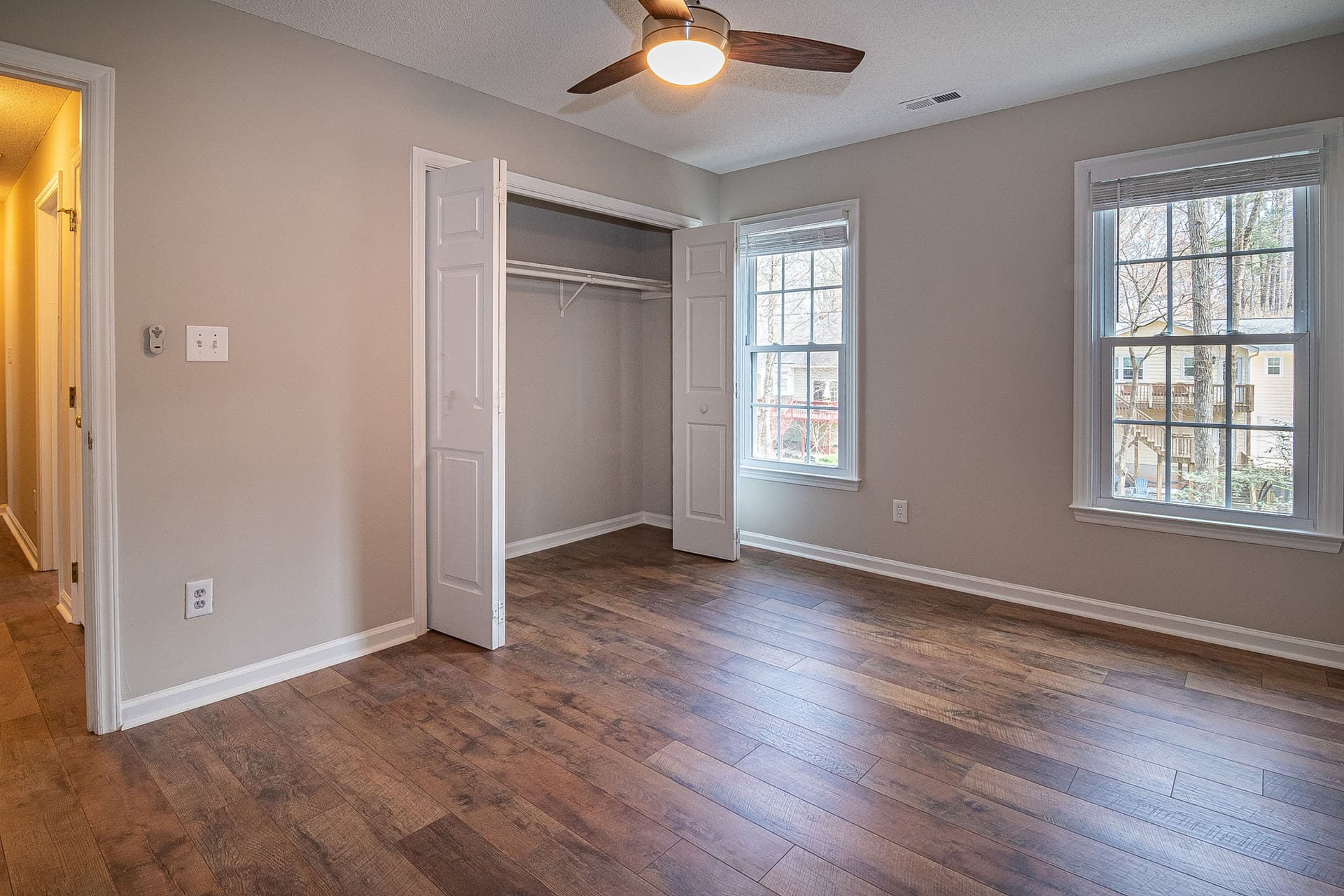 An empty bedroom with a wooden floor, a ceiling fan and an open closet