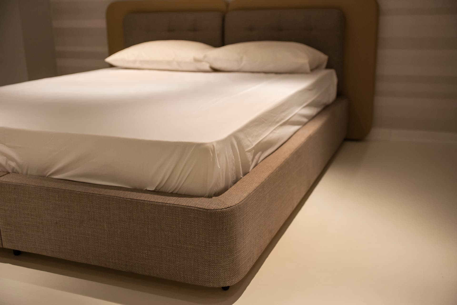 A bed with white linen sheets and pillows in a minimal bedroom, seen from its corner